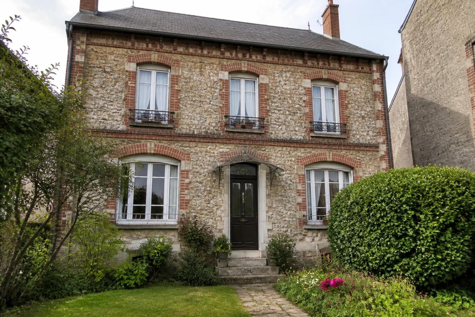 Façade d'une maison meulière ancienne en pierre calcaire avec encadrements en brique